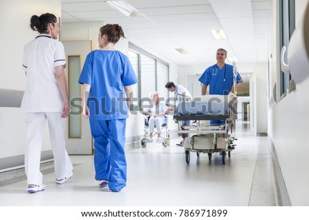 Male nurse pushing stretcher gurney bed in hospital corridor with doctors & senior female patient Royalty-Free Stock Photo #786971899