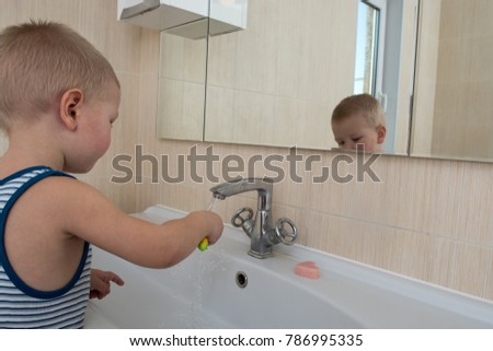 Happy boy taking bath in kitchen sink. Child playing with foam and soap bubbles in sunny bathroom with window. Little baby bathing. Water fun for kids. Hygiene and skin care for children. 