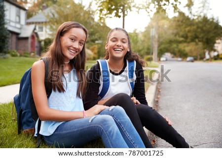 Two teen girlfriends sit at the roadside looking to camera Royalty-Free Stock Photo #787001725