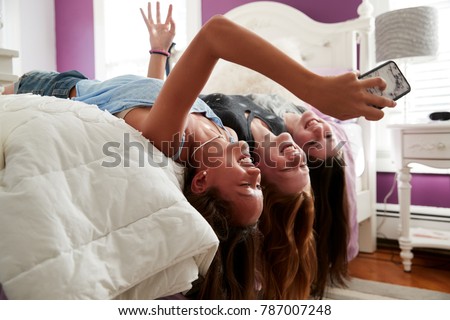 Three teenage girls lying on bed taking a selfie upside down Royalty-Free Stock Photo #787007248