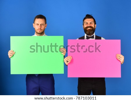 Men with beards hold boards on blue background. Advertisement or commercial posters. Businessmen with serious and happy faces hold green and pink boards, copy space. Announcement or promotion concept