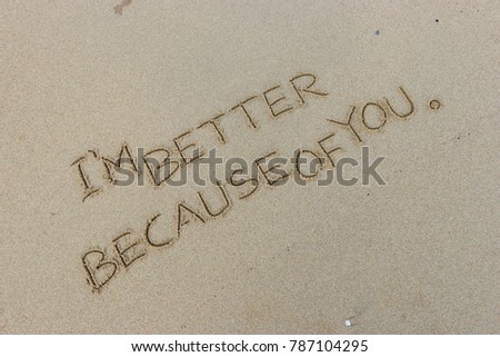 Handwriting  words "I'M BETTER BECAUSE OF YOU." on sand of beach.