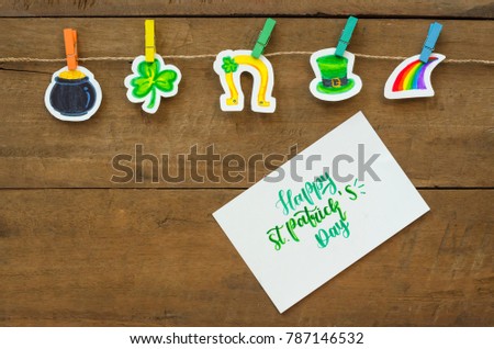 Happy St.Patrick's day greeting card concept with doodles symbols of Irish tradition, cauldron gold pot, clover or shamrock green leaf, Leprechaun hat, horse shoe and rainbow on wood background.
