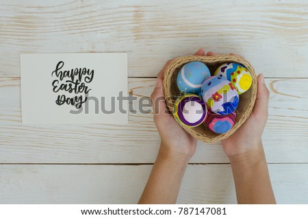 Happy Easter day with hands holding colorful Paschal Easter eggs in heart shaped basket symbolizing Jesus resurrection, springtime celebration and fertility on bright yellow wood table background 