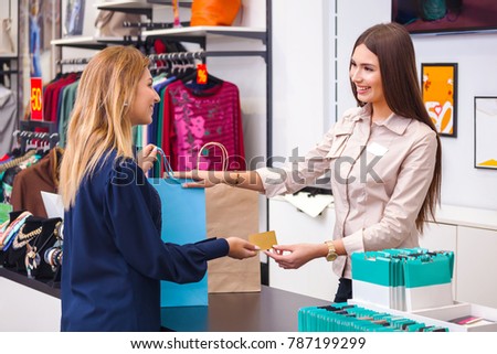 Beautiful young woman with shopping bag giving her credit card to seller in clothing shop Royalty-Free Stock Photo #787199299