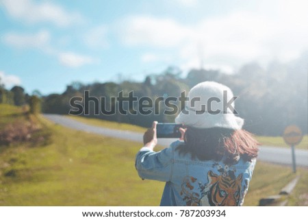 Woman taking photo of road and forest at  mountain against blue sky and clouds with sunshine on smartphone. Selective focus.