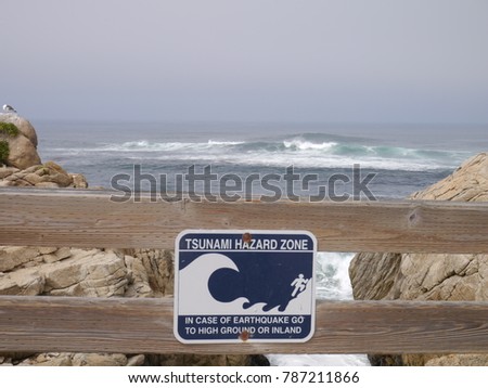Tsunami hazard zone sign on wood fence on California coast with waves and ocean background