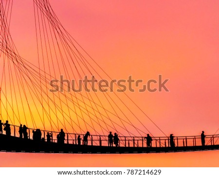 Silhouettes of tourist team on a high bridge enjoying the view from the bridge at dusk.
