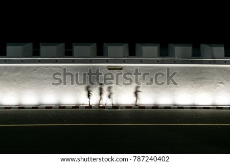 The silhouette picture of the White wall of Grand Palace in Bangkok, Thailand with people walking pass the wall with the name tag of the wall in Thai language