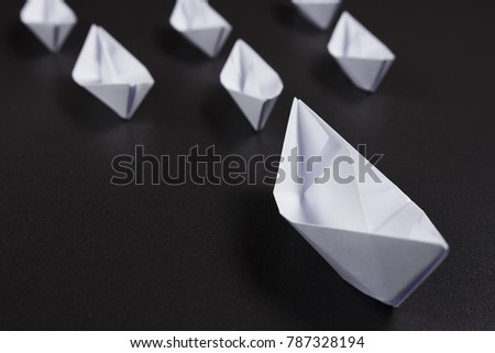 Concept of leadership in business. Origami white ships made of paper on black background. Many small ships are sailing for great leader