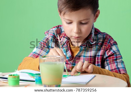 Caucasian boy is carefully painting with watercolors.