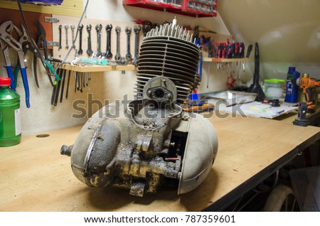 The old and dirty engine from Czech motorbike before renovation with blurred tools in background.