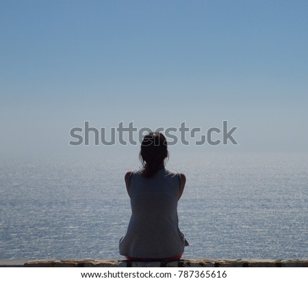 Silhouette of a young woman sitting alone and watching the Aegean Sea , Greece
