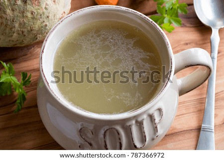 Bone broth made from chicken in a soup bowl, with celery root and parsley in the background