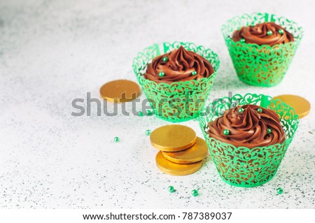 St. Patrick's Day party table: Chocolate cupcakes with green sugar sprinkles near golden coins on light background with blank space for text; selective focus