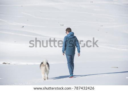 Young man walking with his dog on the snowy field