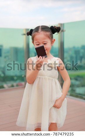 Child girl in cream dress hold and looking photo in her hands at the rooftop of building.