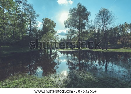 high water level in river Gauja, near Valmiera city in Latvia. summer trees surrounding and reflections of white clouds - vintage film look