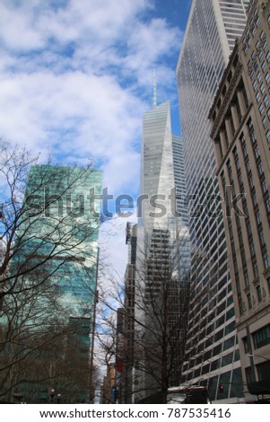 Midtown Manhattan skyscrapers and buildings as seen from Bryant Park, on a a winter day. New York Building reflection and trees silhouette.  blue and white clouds in the background.