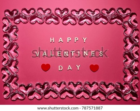 Happy Valentine’s Day made of a wooden letters with a wooden red hearts and a glass hearts frame on a pink background