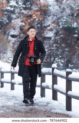 Asian young man taking pictures in winter snow field park Tourist.
