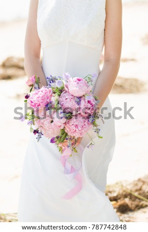 Bride on the beach. Woman holding bouquet of peony flowers.