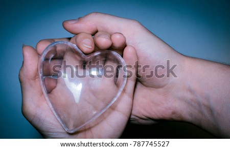 glass heart in women's and men's hand on blue background