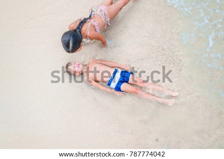 Cute boy and girl  having fun on the sunny tropical beach. Lying on sand, wonderful waves around them. View from above. Copy space, vibrant color concept