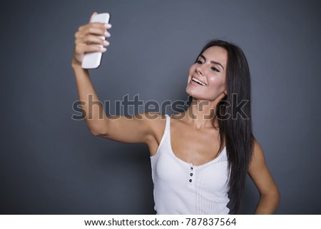 Good camera for photos. Beautiful smiling young modern woman is photographing herself on the phone or doing selfie on a gray background isolated.
