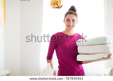 Portrait of the young cheerful woman who standing in the room and holding folded towels in hands