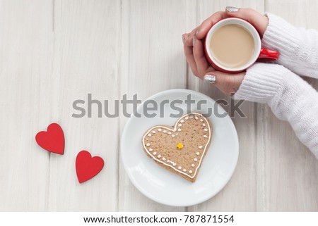 Love concept. Female hands holding a cup of coffee. red hearts and a cookies as a heart in a plate on a wooden table. Top view.