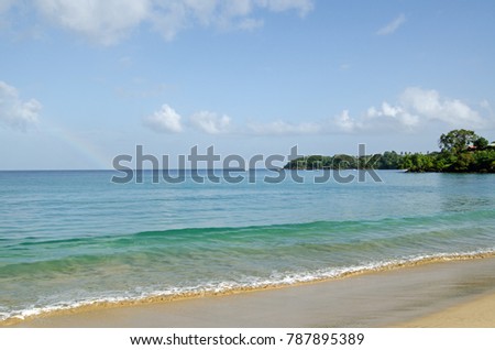 A pale rainbow fades on the horizon during a sunny morning at the beach of Grange Bay, Tobago.  Part of the Caribbean island nation of Trinidad and Tobago.