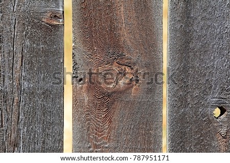 Three  weathered, rough-textured,cedar fence boards with two gaps separating them and forming a strong vertical abstract pattern.  Each board has a knot and one board has a knothole.