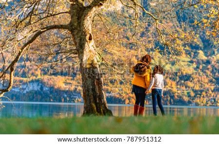 Woman & girl stading under big tree with golden fallen leaves by Brienz Lake, Switzerland in Autumn season