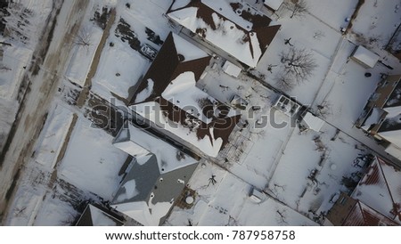 Aerial drone image of the roof of a suburban house in Canada during winter.  Roof and surrounding area is covered with snow.