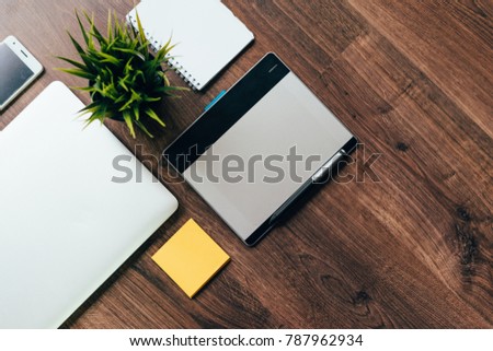 on a wooden floor lie a laptop, a graphic tablet, a white notebook and a green plant