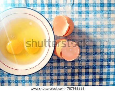 Fresh raw eggs in a bowl at left of image with morning sunshine on old blue and white square pattern floor
