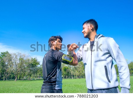 Two Asian athletic friends greeting each other with arm wrestling in the park , friendship concept