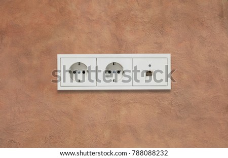 Double modern electric sockets and network line. Light brown stucco wall backdrop. Closeup, details.