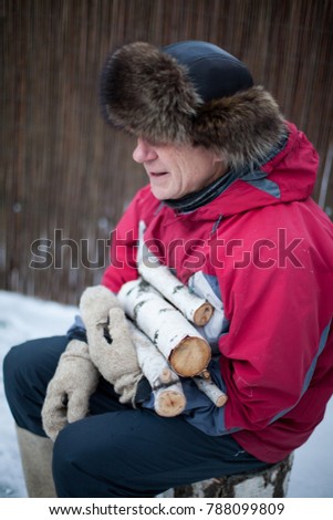 Man in a fur hat and felt boots with birch woods in hands.