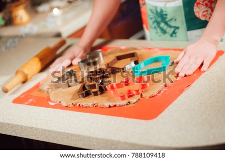 Bakers hands are making a gingerbread house, gingerbread Christmas tree and gingerbread man by using forms on a Christmas tree lights background. Close up. Cooking concept.
