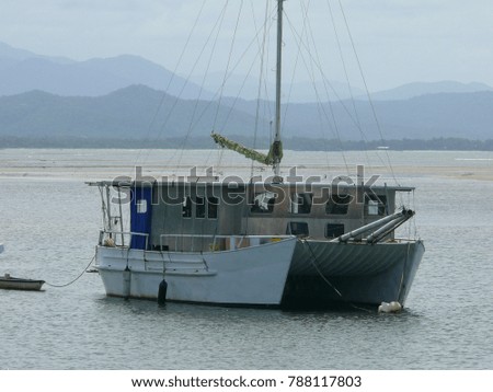 Living catamaran with signs of use , anchoring in a bay with a coast with tropical mountains in the blurry background