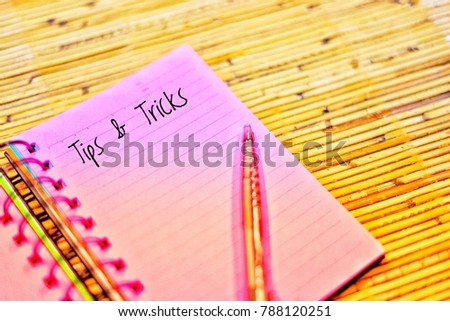 Note book and pen on the bamboo mat written with text Tips and Tricks.