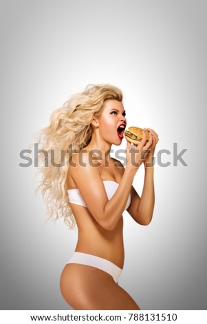 Beautiful pinup model eating a hamburger on grey background.