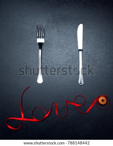 Inscription, word love of red satin ribbon fork and knife.Valentine day background.Love concept.On dark stone background..Creative concept