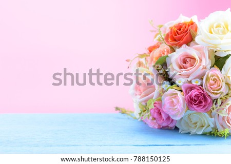 Colorful artificial roses bunch on blue wooden and pink background
