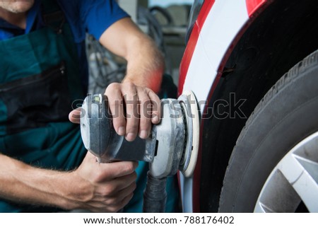 Grinder in the hands of a man who sharpen a car varnish in the car shop. Royalty-Free Stock Photo #788176402