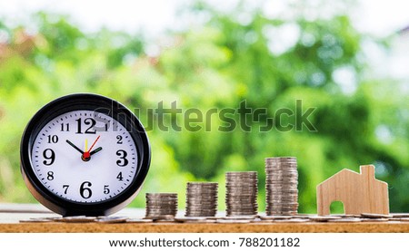 alarm clock and wooden house model and step of coins stacks with nature background, money, saving and investment or family planning concept, over sun flare silhouette tone.