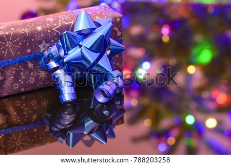 Christmas gift wrapped in purple wrapping paper bound with blue ribbon and ornament. A gift under a decorated tree. Merry Christmas.