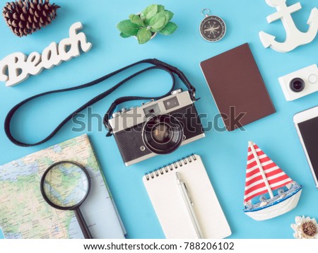 top view travel concept with retro camera films, map, passport, beach wood signs, smartphone, action camera, notebook and outfit on blue background, Tourist essentials